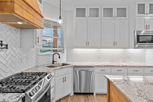 Kitchen featuring stainless steel appliances, exhaust hood, light wood-style flooring, white cabinets, and light stone countertops | Image 11