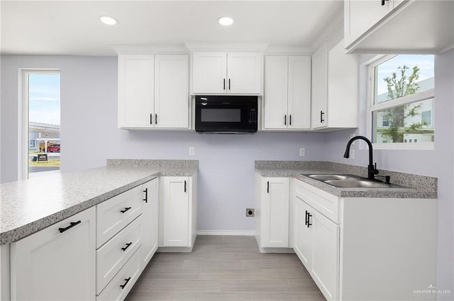 Kitchen featuring black microwave, a sink, recessed lighting, plenty of natural light, and white cabinetry | Image 6