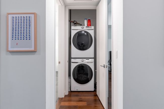 Clothes washing area with stacked washer / drying machine, wood finished floors, and laundry area | Image 26