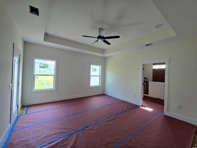 Unfurnished bedroom with a raised ceiling, baseboards, connected bathroom, a ceiling fan, and radiator heating unit | Image 20