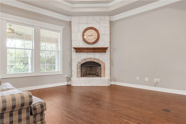 Living room with wood finished floors, a stone fireplace, crown molding, baseboards, and a tray ceiling | Image 6