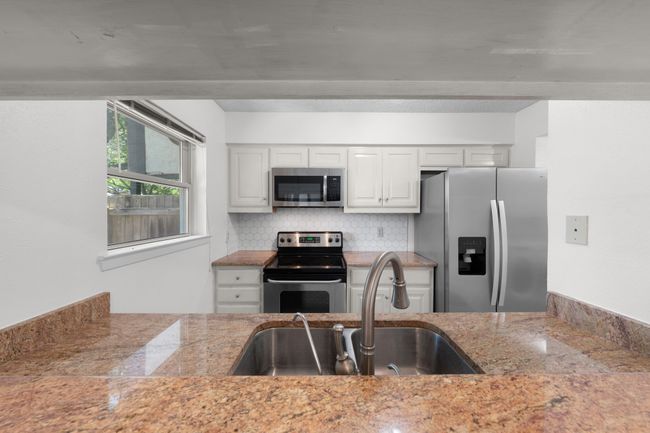 View from dining room into the updated kitchen with granite counters, SS double sink, stainless steel & black appliances, and window overlooking greenbelt. Refrigerator is negotiable. | Image 10