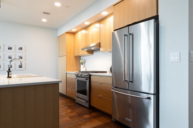 Kitchen with dark wood-style floors, a sink, high end appliances, wall chimney range hood, and light countertops | Image 10