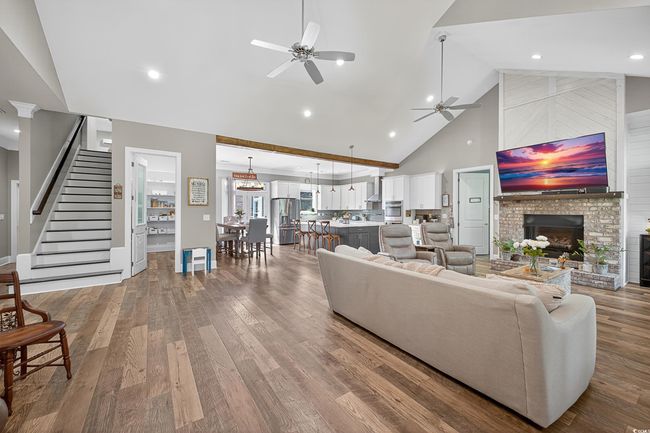Living area featuring high vaulted ceiling, ceiling fan, a large fireplace, stairway, and wood finished floors | Image 9