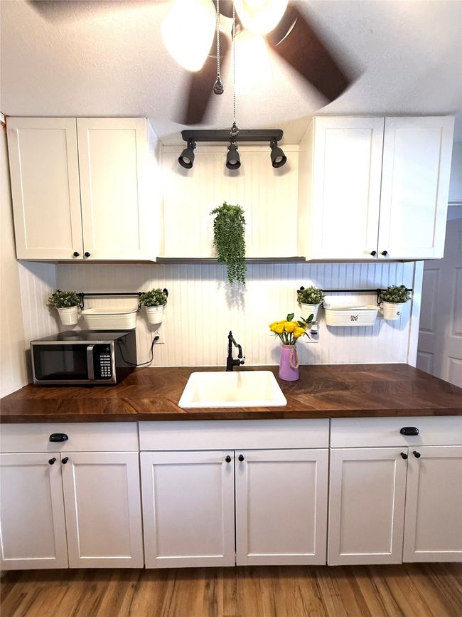 Kitchen with a textured ceiling, butcher block countertops, white cabinets, stainless steel microwave, and light wood-style floors | Image 8