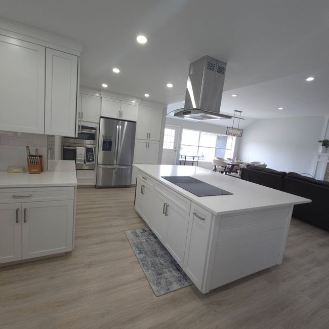 Kitchen featuring stainless steel fridge, island exhaust hood, black electric stovetop, white cabinetry, and recessed lighting | Image 10