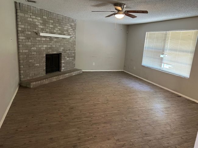 Unfurnished living room featuring a ceiling fan, a textured ceiling, dark wood-style flooring, a brick fireplace, and baseboards | Image 6