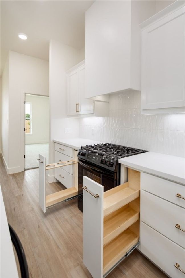 Kitchen with black gas range, white cabinetry, light countertops, light wood-type flooring, and recessed lighting | Image 14