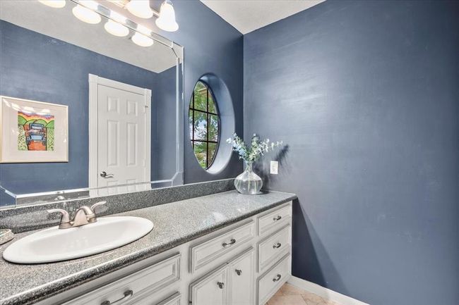 A shared bathroom with navy accent walls, round mirror, and updated vanity brings a bold pop of style to the home’s secondary suite. | Image 27