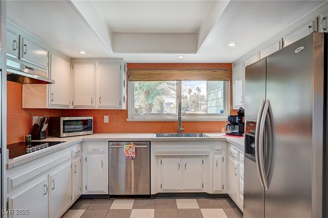Kitchen featuring under cabinet range hood, stainless steel appliances, a sink, light floors, and a raised ceiling | Image 16