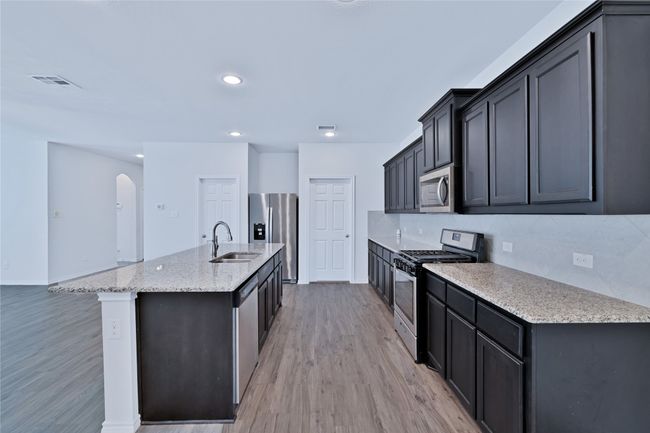 Kitchen with appliances with stainless steel finishes, light wood-type flooring, decorative backsplash, arched walkways, and light stone countertops | Image 9