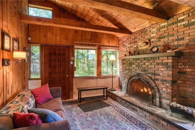 Living room with brick fireplace, wood ceiling, wooden walls, and lofted ceiling with beams | Image 5