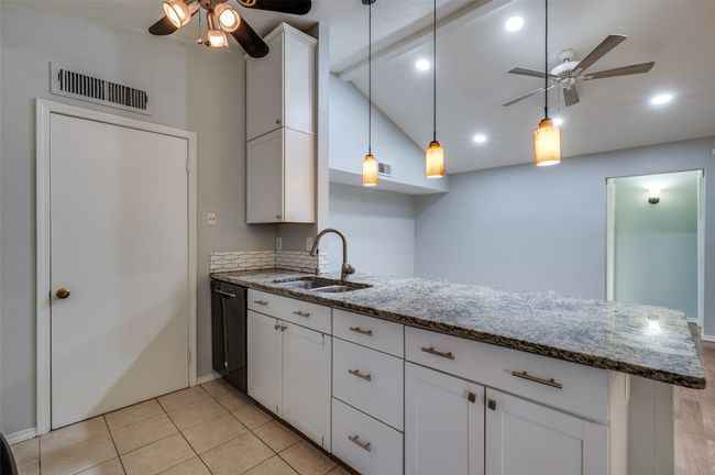 Kitchen featuring ceiling fan, black dishwasher, vaulted ceiling, a peninsula, and white cabinetry | Image 7
