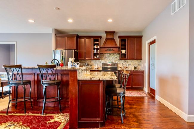 Kitchen featuring visible vents, decorative backsplash, custom exhaust hood, a breakfast bar area, and stainless steel appliances | Image 7