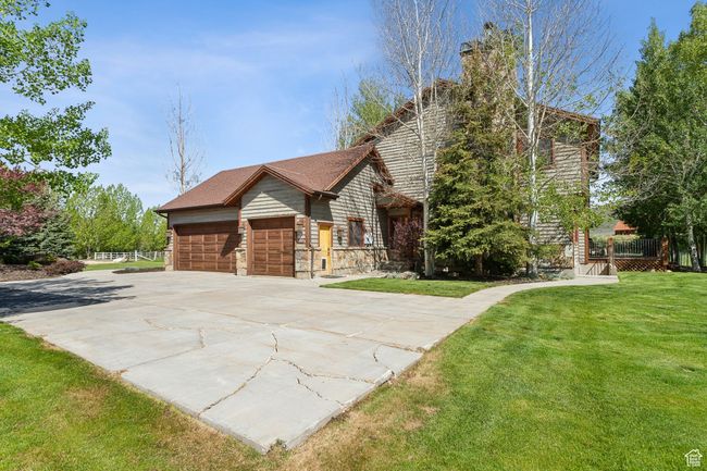 View of front of property featuring a front yard, a garage, driveway, a chimney, and stone siding | Image 57