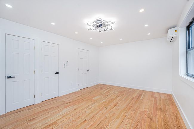 Empty room with an AC wall unit, light wood-style flooring, and recessed lighting | Image 8