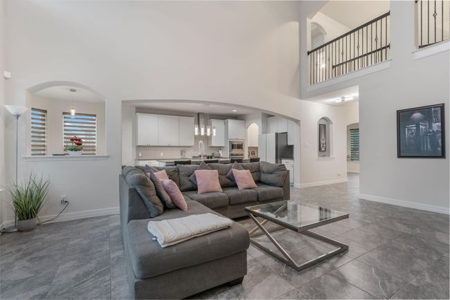 High ceiling living area with a view into the contemporary kitchen with white cabinetry and stainless steel appliances. A balcony overlooks the space, adding elegance and openness. | Image 11
