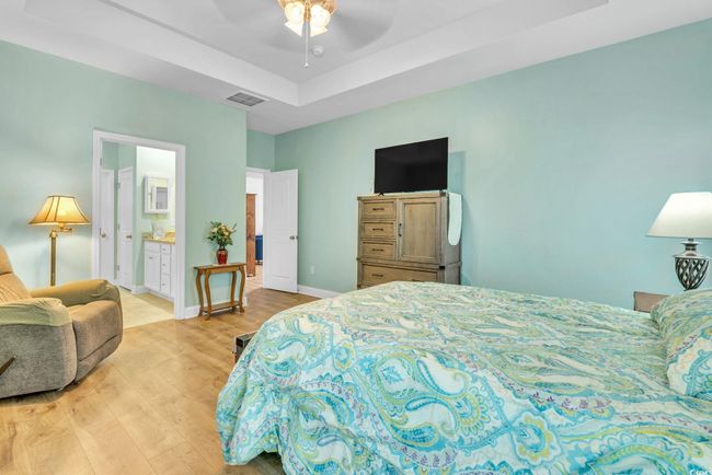 Bedroom with connected bathroom, a tray ceiling, light wood-style flooring, visible vents, and baseboards | Image 13