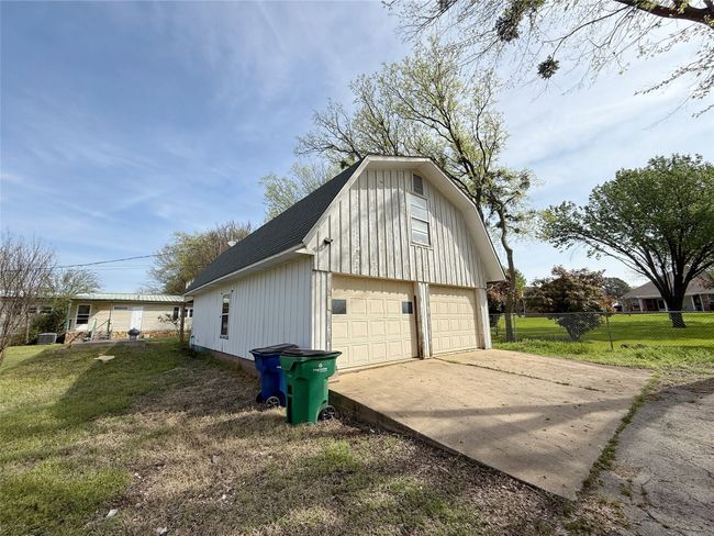 View of property exterior featuring a gambrel roof, fence, a shingled roof, a lawn, and a garage | Image 19