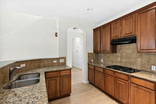 Kitchen featuring under cabinet range hood, black gas cooktop, light stone counters, backsplash, and light wood-style floors | Image 12