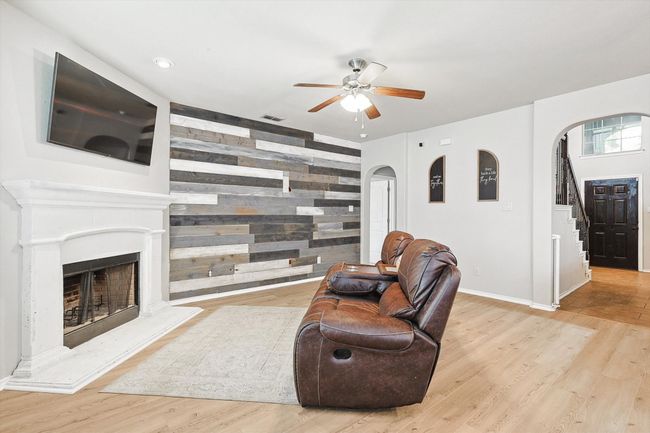 Living room featuring arched walkways, a ceiling fan, wood finished floors, stairway, and a fireplace with raised hearth | Image 10