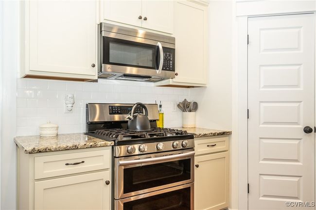 Kitchen featuring backsplash, light stone countertops, stainless steel appliances, and white cabinetry | Image 14