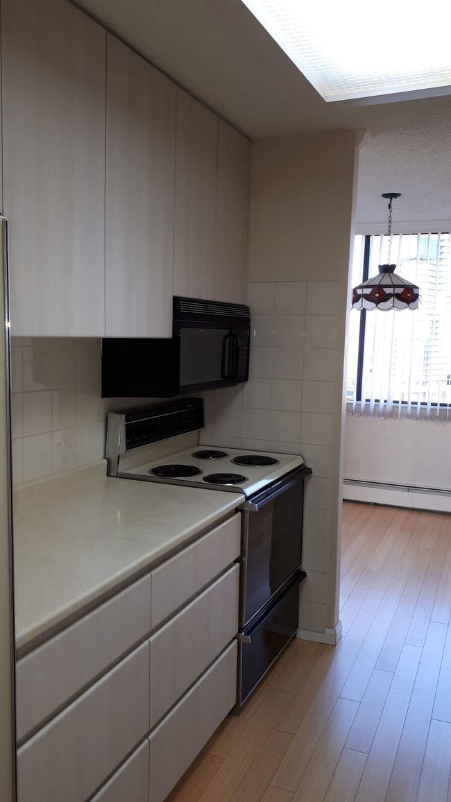 Kitchen featuring range with electric cooktop, black microwave, light countertops, light wood-style flooring, and a baseboard radiator | Image 16