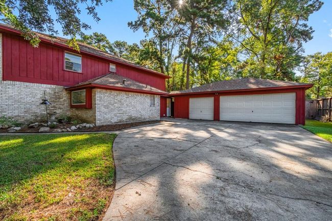 This is a two-story home featuring a red and white exterior with a spacious three-car garage and a wide driveway, set against a backdrop of mature trees. | Image 4