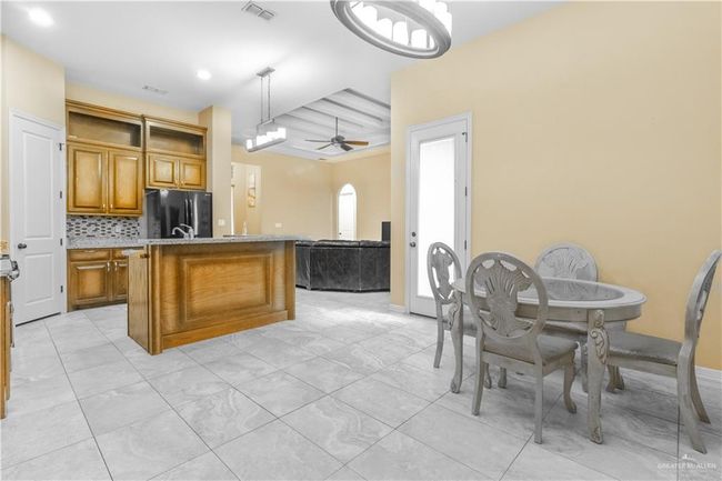 Kitchen with beam ceiling, hanging light fixtures, a center island with sink, stainless steel refrigerator, and tasteful backsplash | Image 4