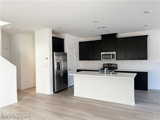 Kitchen with an island with sink, granite countertops, stainless steel appliances, dark cabinetry, and light wood finished floors | Image 5