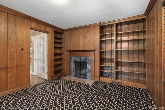 Unfurnished living room with wood walls, ornamental molding, a tile fireplace, carpet, and built in shelves | Image 12