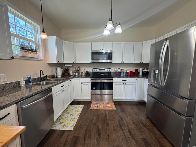 Kitchen with appliances with stainless steel finishes, a chandelier, dark wood-style floors, a sink, and white cabinets | Image 10