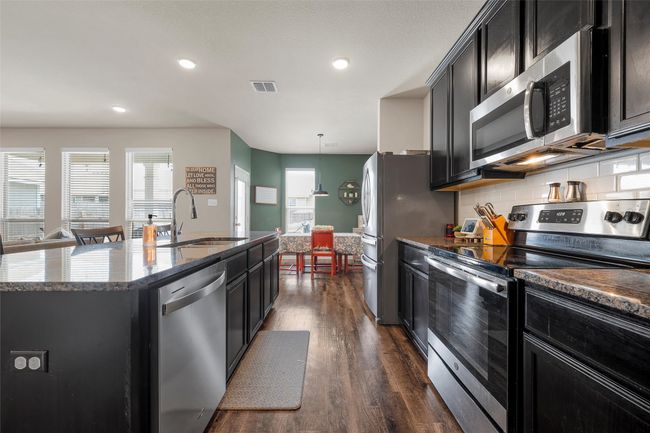 Kitchen with stainless steel appliances, dark cabinets, dark wood-type flooring, an island with sink, and dark stone countertops | Image 6