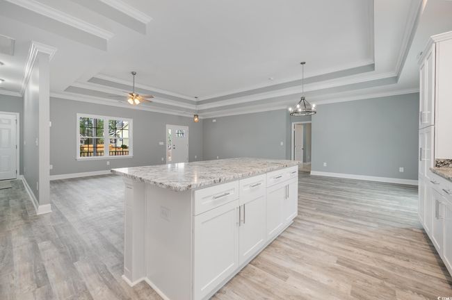 Kitchen featuring ceiling fan with notable chandelier, a center island, white cabinetry, and a tray ceiling | Image 8