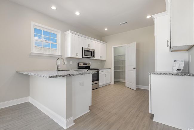 Kitchen featuring kitchen peninsula, stainless steel appliances, sink, light hardwood / wood-style floors, and white cabinetry | Image 14