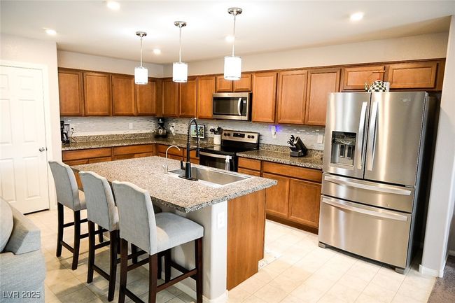 Kitchen featuring a kitchen breakfast bar, a sink, brown cabinetry, pendant lighting, and appliances with stainless steel finishes | Image 9