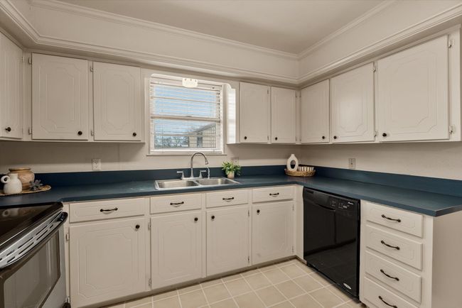 Kitchen with sink, crown molding, white cabinetry, black dishwasher, and light tile patterned flooring | Image 13