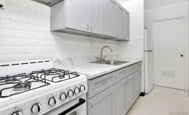 Kitchen featuring white appliances, tasteful backsplash, light tile patterned floors, and light stone counters | Image 6