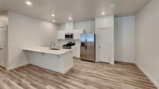 Kitchen with tasteful backsplash, appliances with stainless steel finishes, light wood finished floors, a sink, and a peninsula | Image 6