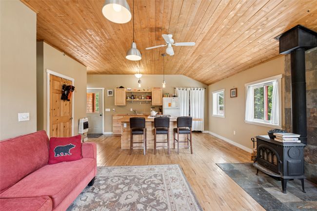 Apartment living area with a wood stove, wood ceiling, lofted ceiling, light wood-type flooring, and a ceiling fan | Image 52