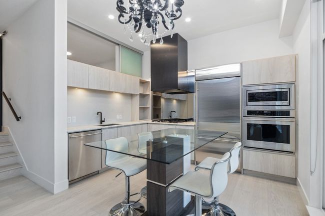 Kitchen with light countertops, range hood, modern cabinets, a sink, and built in appliances | Image 9