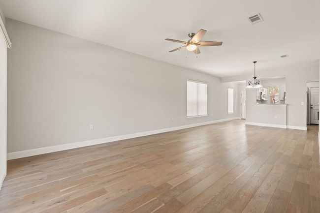 Unfurnished living room featuring light wood-type flooring, ceiling fan with notable chandelier, baseboards, and visible vents | Image 10