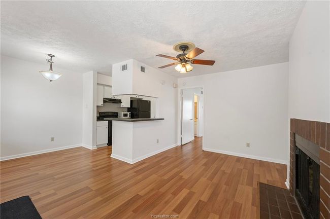 Unfurnished living room featuring a tiled fireplace, light wood-style floors, a textured ceiling, and ceiling fan | Image 4