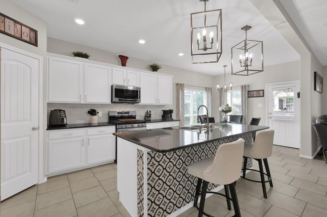 The kitchen boasts crisp white cabinetry, modern lighting, and a large island with eye-catching patterned tile and seating space. | Image 8
