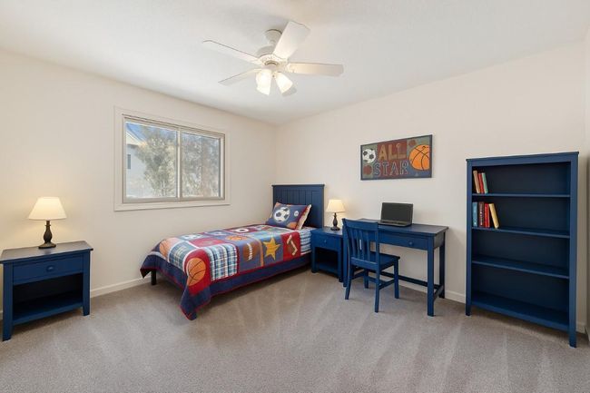 Upper Level Bright and playful boy’s bedroom (3rd) featuring matching blue furniture, a nightstand with a lamp, study desk with a laptop, and a bookshelf with neatly arranged books. (virtually staged) | Image 20