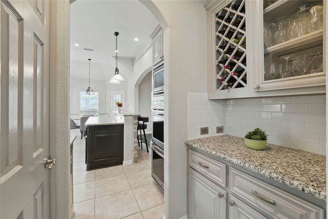 Kitchen featuring arched walkways, decorative backsplash, light tile patterned floors, hanging light fixtures, and light stone counters | Image 9