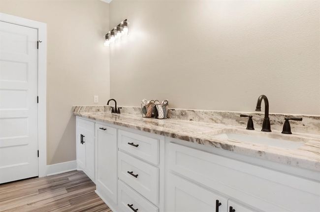 This photo showcases a modern bathroom with a double vanity featuring marble countertops and dark fixtures. The cabinetry is white with ample storage, and the lighting is stylishly contemporary, creating a bright and inviting space. | Image 19