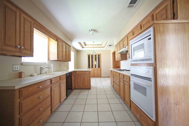 Kitchen featuring white appliances, a sink, a peninsula, light tile patterned flooring, and brown cabinets | Image 6