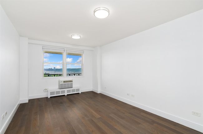 Empty room with dark wood finished floors, radiator heating unit, and an AC wall unit | Image 8