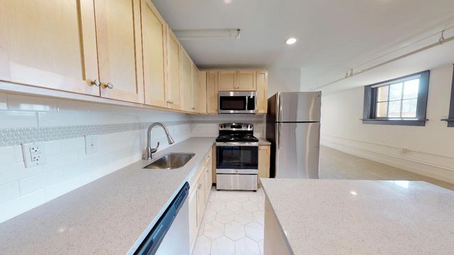 Kitchen featuring light brown cabinets, tasteful backsplash, light stone countertops, appliances with stainless steel finishes, and sink | Image 5